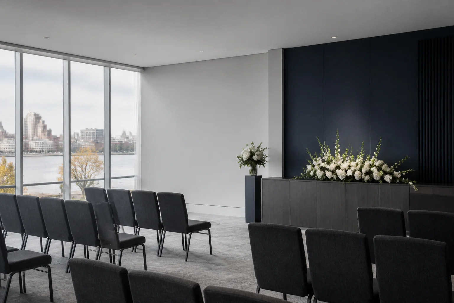 An empty memorial gathering room with daylight, gray chairs, and white flowers
